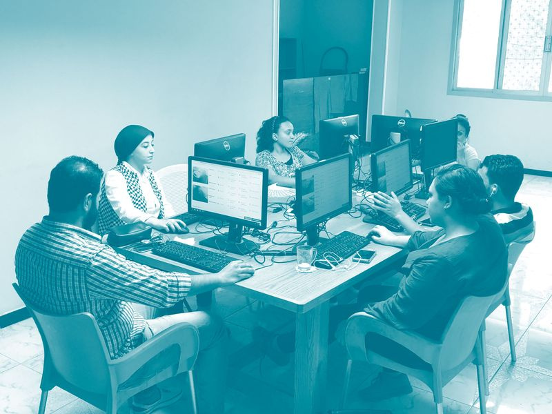 Remote-Mitarbeiter in Kairo arbeiten an Desktop-Computern um einen Tisch herum