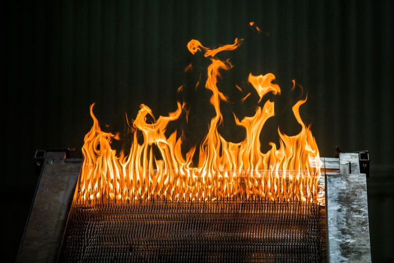 Ein Bild von Little Bertha, das mit hochzellulosem Karton und MDF verpackt ist. Wenn der Karton und MDF brennen, zeigt es die Ausbreitung des Feuers einen Hang hinauf und zeigt auch eine sehr spezifische U-Formation, die die Flammen annehmen.