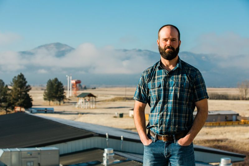 Foto von Jason, der auf dem Dach des Missoula Fire Lab steht, mit Rauchspringerausrüstung hinter ihm.