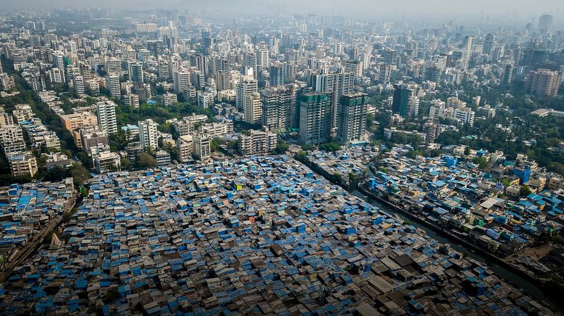 Teile von Mumbai gehören zu den am dichtesten besiedelten Gebieten der Erde. An einigen Orten leben mehr als eine Million Menschen auf weniger als einer Quadratmeile. Dicht gepackte Gebäude, größtenteils aus grauem Beton, bedeckt mit blauen Planen, schützen vor dem Monsunregen.