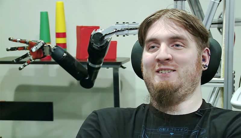 Portrét Nathana Copelanda, jednoho z prvních lidí, kteří měli mozkové počítačové rozhraní, s robotickou paží za hlavou
