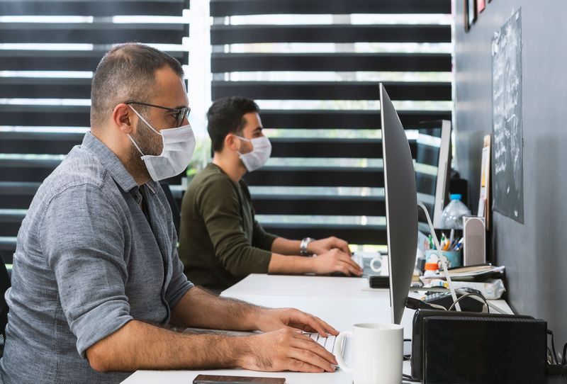 Dva podnikatelé s ochrannými maskami pracují v kanceláři