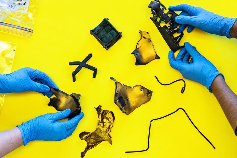 Foto von zwei Personen mit Handschuhen, die Weltraumschrott auf einer gelben Tischplatte untersuchen