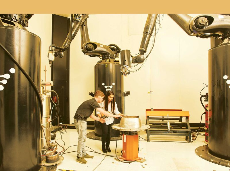 Zwei Personen arbeiten neben Roboterarmen aus dem 3D-Drucker
