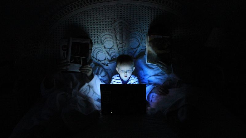 Un enfant est assis entre ses parents distraits, captivé par ce qu