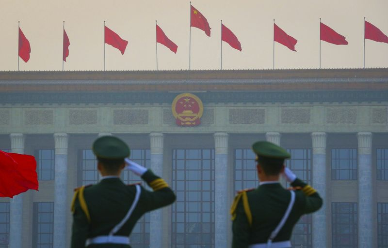 Chinesische paramilitärische bewaffnete Polizisten grüßen, während rote Fahnen vor der Großen Halle des Volkes in Peking flattern.