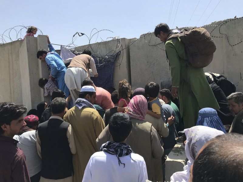 Menschen kämpfen, um die Begrenzungsmauer des internationalen Flughafens Hamid Karzai in Kabul zu überqueren.